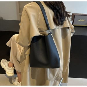 Detail of black lychee grain leather tote bag with gold hardware worn by a model