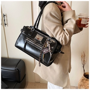 Detail of black glossy leather tote bag with silver logo plaque and decorative keychain