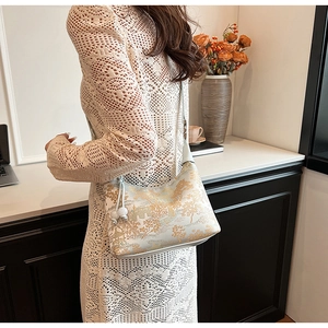 Detail of white half-moon shoulder bag with golden traditional Chinese pattern and slim strap