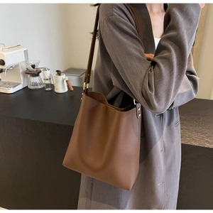 Detail of dark brown pebbled leather bucket bag with metallic rivet accents on side