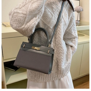 Detail of a dark grey trapezoidal handbag with gold twist lock on a beige outfit background