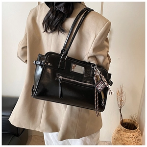 Detail of black glossy shoulder bag with mini Holy Bible charm and metal zipper