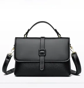 Detail of dual-texture black leather messenger bag with white stitching and gold hardware