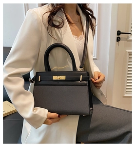 Detail of minimalist black handbag featuring a golden metal buckle and sleek leather texture