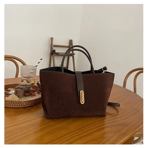 Detail of dark brown frosted leather tote bag with gold buckle on a wooden table