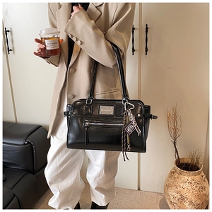 Detail of black glossy tote bag with silver logo plate and decorative book pendant