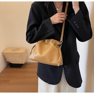 Vue détaillée du sac seau plissé jaune moutarde avec logo et texture en cuir souple