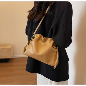 Détail du sac seau en cuir marron clair avec nœuds latéraux et texture lisse