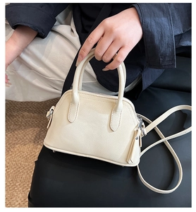 Detail view of cream shell bag with lychee texture, handles, and leather tassel charm