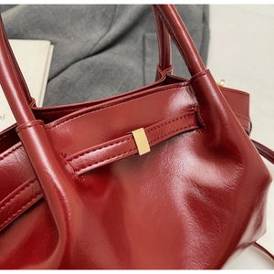Gros plan sur un cabas bordeaux en cuir brillant avec grain fin et boucle en métal doré