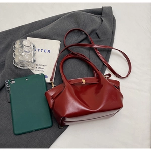 Détail du sac cabas en cuir verni bordeaux avec plis et boucle dorée sur un blazer