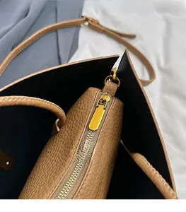 Close-up of brown litchi grain leather tote bag featuring gold polished hardware zippers