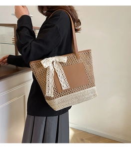Close-up of woven straw tote bag with lace bow decoration and brown leather shoulder strap