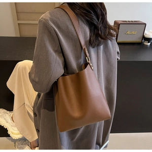 Close-up of brown lychee leather bucket bag with golden hardware on a female model