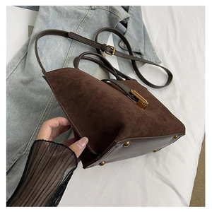 Detail of dark brown suede and leather bucket bag with gold hardware on denim background