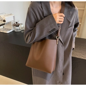 Detail of brown lychee-textured leather bucket bag with wide shoulder strap and gold buckle