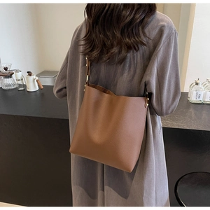 Detail of dark brown pebble leather texture and gold hardware on a minimalist tote bag