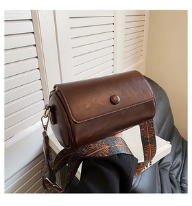 Detail of dark brown cylinder bag with colorful vintage geometric wide shoulder strap