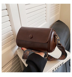Detail of dark brown cylinder bag featuring a retro jacquard strap and gold hooks