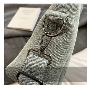 Close-up of gunmetal hardware hooks and buckles on a light blue denim tote bag