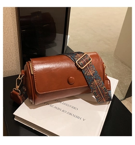 Close-up of brown vintage cylinder bag with ethnic patterned wide woven strap on a book