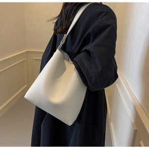 Side view of white lychee leather bucket bag worn by model in a minimalist interior