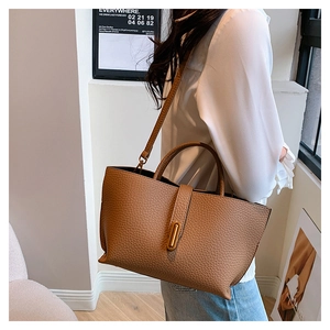Detailed shot of brown litchi pattern tote bag with gold buckle on casual outfit