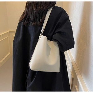 Detail of cream pebbled leather tote with gold hardware on a model in a dark coat