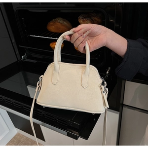 Detail of beige textured shell bag with round handles and adjustable shoulder strap