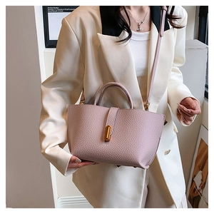 Detail view of pink lychee leather tote bag with elegant gold clasp on white blazer