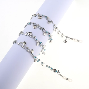 Silver eyewear chain with shell charms and blue crystals on white cylindrical display