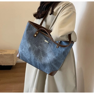 Dettaglio della borsa tote in tela blu-grigia con finiture in pelle e accenti dorati su modella
