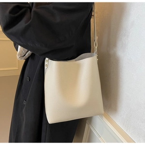 Close-up of beige lychee grain leather bucket bag with gold rivets and adjustable strap