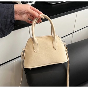 Detailed view of beige mini crossbody bag showing lychee leather texture and metal protective feet