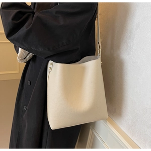 Detail of cream white bucket bag showing pebbled leather texture and gold metal rivets