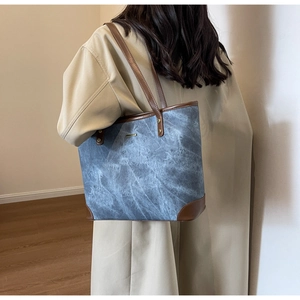 Dettaglio borsa tote in denim con finiture in pelle e borchie dorate indossata da modella