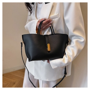 Detail of black lychee grain leather tote bag with gold oval buckle and white blazer