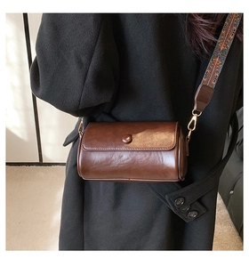 Detail of a brown cylindrical crossbody bag with retro patterned wide shoulder strap