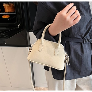 Macro view of beige lychee pattern faux leather handbag with metal zipper and rounded handles