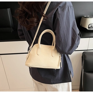 Close-up of a cream shell bag with textured leather and metal protective base studs