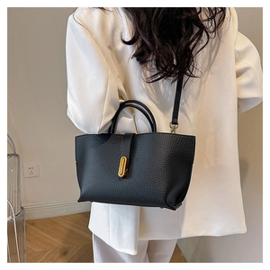 Close-up of black lychee texture leather tote with golden buckle on white blazer