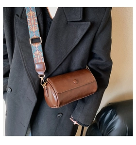 Detailed view of vintage brown cylinder bag with bohemian colorful wide strap on coat