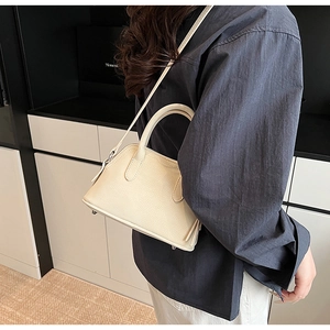Detailed side view of off-white lychee grain leather shell bag with top handles and strap