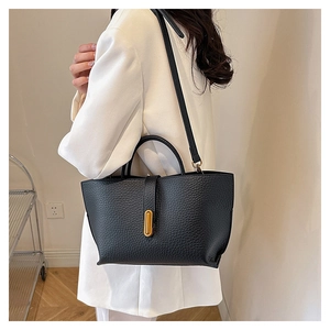 Detail view of black lychee leather tote bag with gold buckle on a white blazer