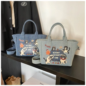 Detail view of denim tote bags featuring cartoon cat illustrations and adjustable straps