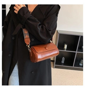 Detail of brown cylinder bag showing ethnic embroidered wide strap on a black coat