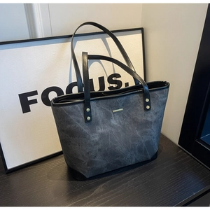 Dettaglio borsa tote grigio scuro con finiture dorate su piano in legno scuro