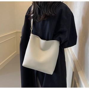Detail of white lychee pattern leather bucket bag worn by model in minimalist indoor setting