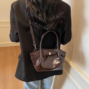 Détail d'un sac cabas en cuir verni marron brillant montrant la surface et les finitions argentées