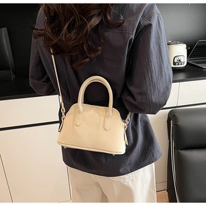 Detailed view of cream leather shell bag with twin handles and bottom protective studs